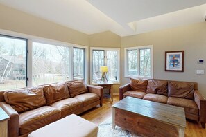 A living room with leather sofas, a wooden coffee table, and large windows. - Ski-in/out home with a hot tub, fireplace, cable & golf nearby (Ludlow)