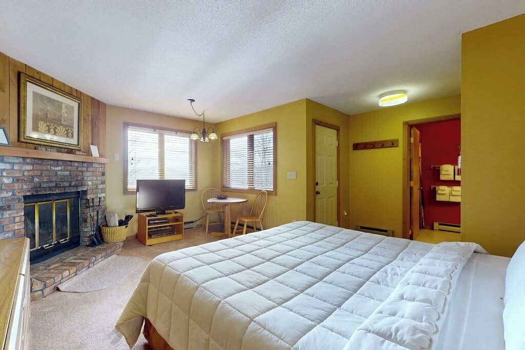 A bedroom with a large bed, a fireplace, a television, and a dining area.