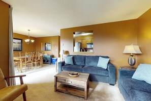 A living room with a sofa, coffee table, and a dining area with chairs and a table. - Ski-in/out Condo on Bull Run Trail with fireplace, & full kitchen (Ludlow)