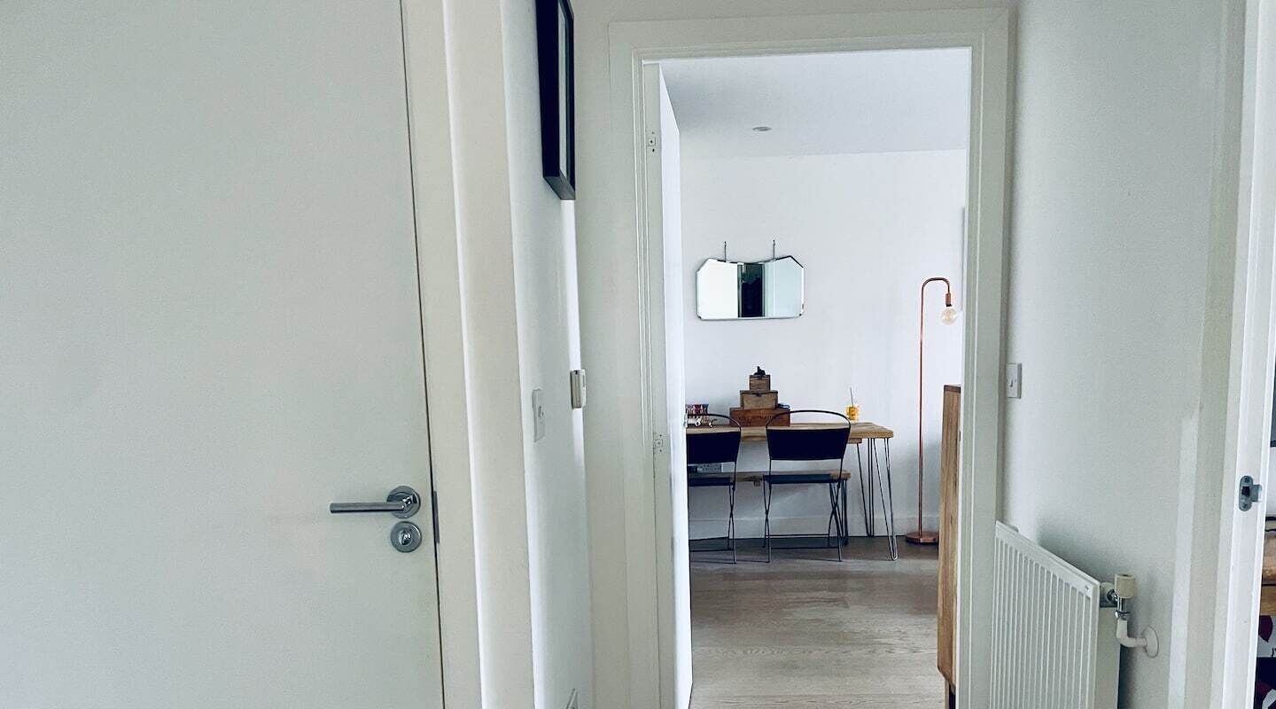 En dörröppning leder in till en matplats med ett bord och stolar, en spegel på väggen och ett element på väggen.