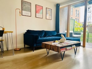 A modern living room with a blue sofa, a wooden coffee table, and a cityscape view through large windows. - Entire rental unit in London, United Kingdom (London)