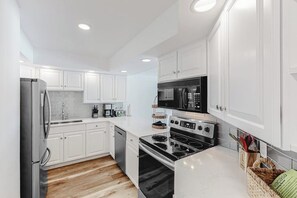 Eine moderne Küche mit weißen Schränken, einem Edelstahlkühlschrank, einer Mikrowelle, einem Backofen und einem Geschirrspüler.