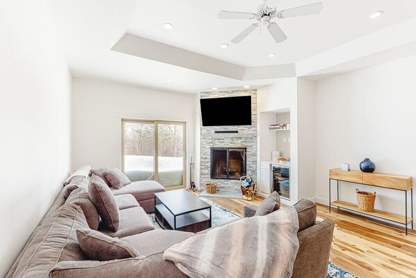 A modern living room with a sofa, coffee table, fireplace, television, and a ceiling fan. - Ski-in/out condo with fireplace, pool, hot tub, sauna & washer/dryer (Ludlow)