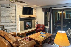 Ein Wohnzimmer mit Kamin, Ledersofa und einem darüber hängenden Fernseher.