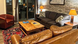 Ein Wohnzimmer mit einer Ledersofa, einem Holztisch, einem roten Sessel und einem gemusterten Teppich.