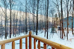 A wooden deck with a view of a snowy forest and a building in the background. - Beautiful home near lifts with wood-burning fireplace, mountain views & cable (Ludlow)
