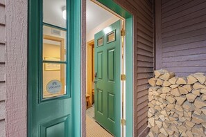 Eine grüne Tür mit Fenster, ein Holzstoß und ein sichtbarer Innenraum mit einer Lampe.