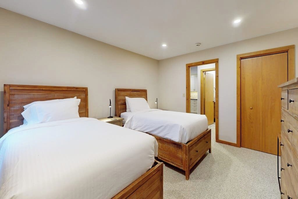 A bedroom with two beds, wooden headboards, a dresser, and a door leading to another room.