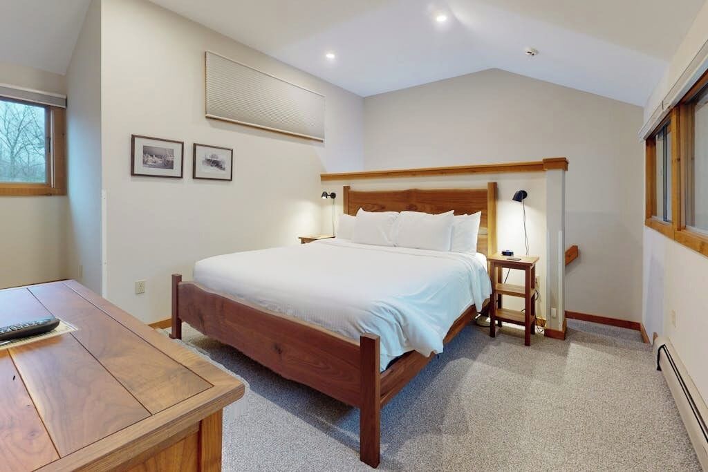 A bedroom with a wooden bed, bedside tables, a nightstand, a desk, and a window.