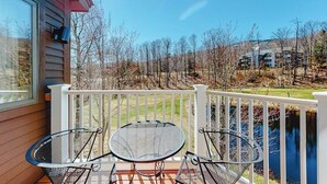 Un balcon avec une table et des chaises, une balustrade et une vue sur les arbres et les bâtiments.