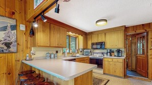 Una cocina con armarios de madera, una isla central con taburetes, un microondas y un refrigerador.