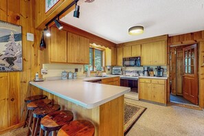 A kitchen with wooden cabinets, a central island with stools, a microwave, and a refrigerator. - Inviting Okemo ski mountain home, two house walk to ski slope! (Ludlow)