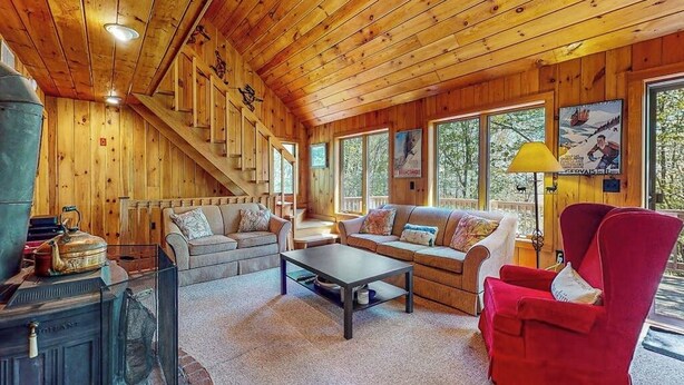 Interior de una cabaña de madera con sofá, sillón, mesa de centro y chimenea.
