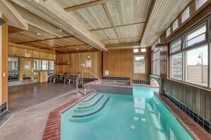 Ein Innenpool mit Holzboden und -wänden, ein Sitzbereich mit Tischen und Stühlen sowie ein Blick durch große Fenster.