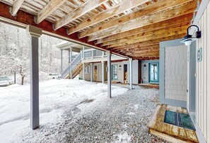 Ein überdachter Außenbereich mit Holzboden, einer Treppe zu einem zweiten Stockwerk und einer Tür mit Fenster.