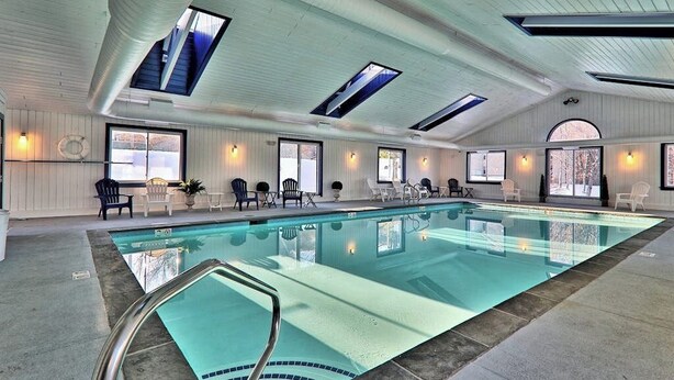 Ein Schwimmbad mit freiem Blick zum Himmel durch Dachfenster, umgeben von Stühlen und einem sonnendurchfluteten Innenraum.