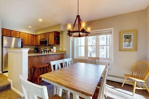 A kitchen with wooden cabinets, a stainless steel refrigerator, a wooden dining table with chairs, and a chandelier. - Winterplace ground-floor ski-in/ski-out condo on the Lift Line trail (Ludlow)