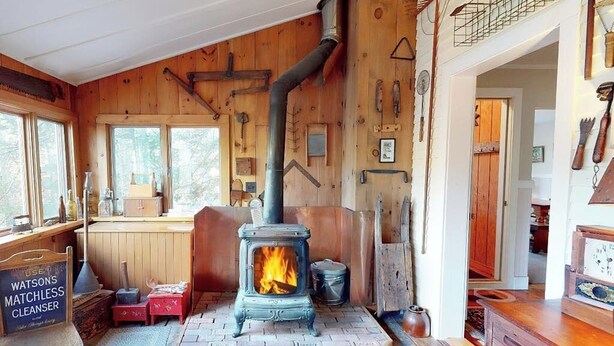 Een landelijk blokhutinterieur met een houtkachel, houten wanden, een raam en een houten bank.