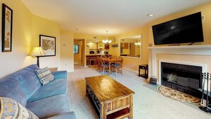 Una sala de estar con sofá, mesa de centro, chimenea, televisor y comedor.