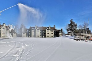 A snow-covered street with buildings, a clear sky, and a snow blower in action. - Ski-in/out condo with fireplace, hot tubs. pool, tennis & washer/dryer (Ludlow)