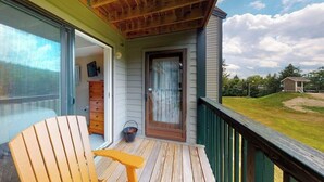 Una terraza de madera con un ventanal corredero que da a una habitación con un aparador y una silla.