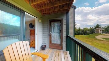 A wooden deck with a sliding glass door leading to a room with a dresser and a chair.
