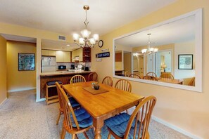 A dining area with a wooden table and chairs, a kitchen in the background, and a large mirror on the wall. - Ski-in/out condo with fireplace, hot tubs. pool, tennis & washer/dryer (Ludlow)
