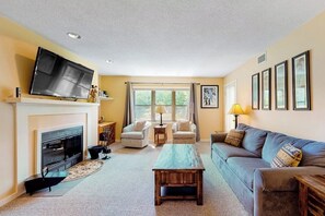 A living room with a fireplace, a television, a sofa, and a coffee table. - Ski-in/out condo with fireplace, hot tubs. pool, tennis & washer/dryer (Ludlow)