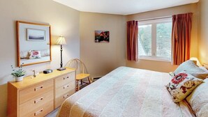 Une chambre à coucher avec un lit, une commode, une chaise, une lampe et une fenêtre avec des rideaux.