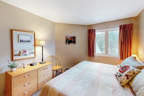 Un dormitorio con cama, cómoda, silla, lámpara y ventana con cortinas.