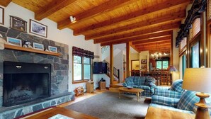 Una sala de estar acogedora con chimenea de piedra, vigas de madera en el techo, un sofá y un televisor.