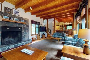 Ein gemütliches Wohnzimmer mit Kamin aus Stein, Holzbalkendecke, einer Couch und einem Fernseher.