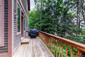 Eine Holzdielen-Terrasse mit überdachtem Grill, Geländer und einem Haus mit Fenster und Tür.