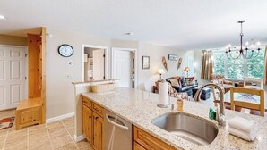 A kitchen with granite countertops, a stainless steel sink, wooden cabinets, and a dining area with a chandelier. - Condo near ski trail with fireplace, hot tub, pool, tennis & washer/dryer (Ludlow)