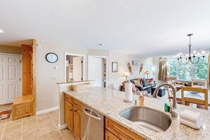 A kitchen with granite countertops, a stainless steel sink, wooden cabinets, and a dining area with a chandelier. - Condo near ski trail with fireplace, hot tub, pool, tennis & washer/dryer (Ludlow)