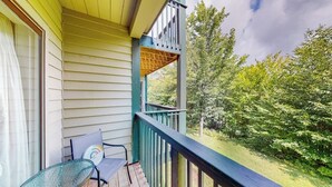 A wooden deck with a glass table and chairs, a balcony with a railing, and a view of trees. - Condo near ski trail with fireplace, hot tub, pool, tennis & washer/dryer (Ludlow)