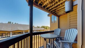 Un terrazzo in legno con due poltrone Adirondack e un tavolino rotondo, con vista su un edificio con tetto spiovente.