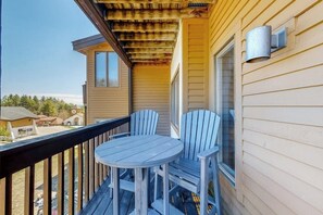 A balcony with a round table and two chairs, a metal light fixture, and a window. - Okemo Mountain Lodge ski-in/ski-out condo with private patio, lifts steps away (Ludlow)