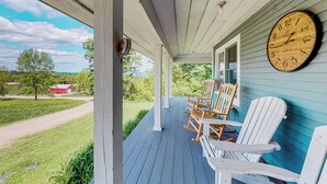 A porch with a clock, Adirondack chairs, and a view of a rural landscape. - Secluded escape on rolling acreage with hot tub, deck, gas grill, & fast WiFi (Ludlow)