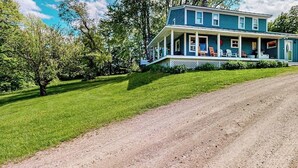 A two-story house with a porch, surrounded by a well-maintained lawn and trees. - Secluded escape on rolling acreage with hot tub, deck, gas grill, & fast WiFi (Ludlow)