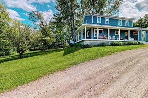 A two-story house with a porch, surrounded by a well-maintained lawn and trees. - Secluded escape on rolling acreage with hot tub, deck, gas grill, & fast WiFi (Ludlow)