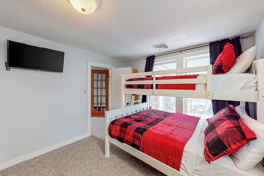 Una camera con un letto a castello, una televisione a parete, una porta con una finestra e un pavimento rivestito di moquette.