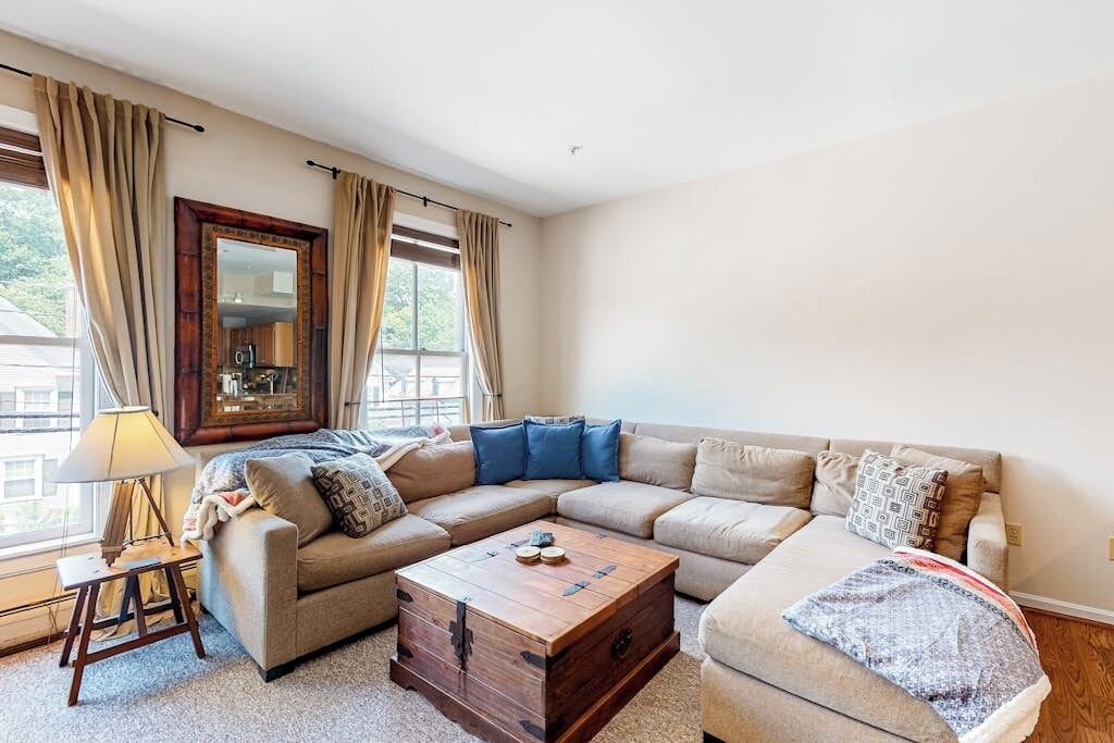 A living room with a sectional sofa, a wooden coffee table, a lamp, and a large mirror.