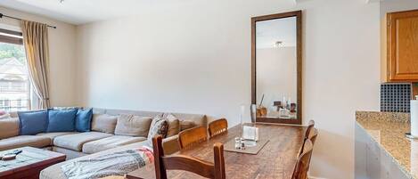 A living room with a sofa, a wooden dining table, and a kitchen area with cabinets.