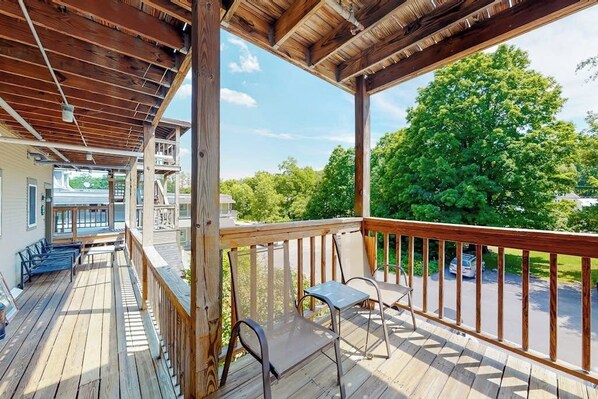 Eine Holzterrasse mit Stühlen und einem Tisch, mit Blick auf einen Parkplatz und Grünflächen.