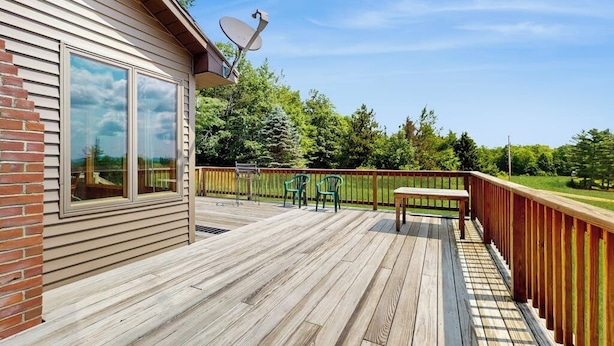 Eine Holzterrasse mit einer Satellitenschüssel, einer Ziegelwand und Blick auf eine grüne Landschaft.