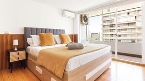 A modern bedroom with a bed, bedside table, and a view of a building through a glass door. - Modern Family Apartment in Las Condes (Las Condes)