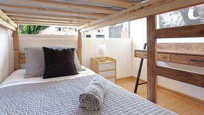 A bedroom with a bed, a nightstand, a desk, and a window overlooking a building. - Modern Family Apartment in Las Condes (Las Condes)