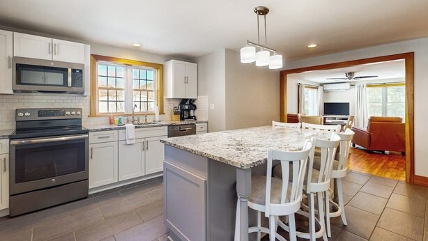 Una cocina moderna con gabinetes blancos, una isla con encimera de granito y un comedor con sillas blancas.