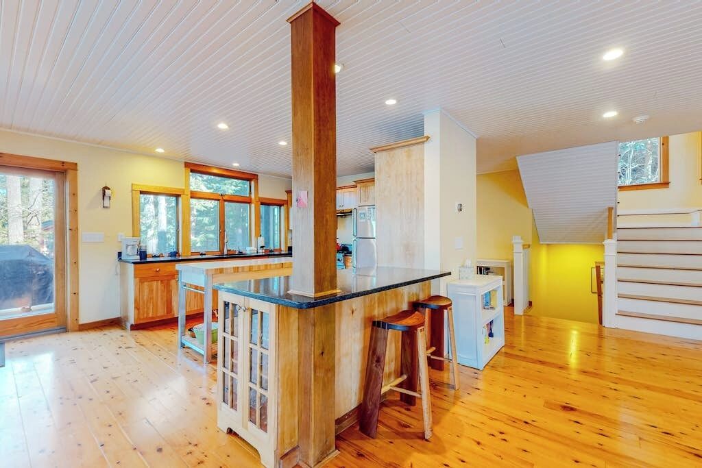 Una cocina amplia con piso de madera, una isla central con taburetes y un ventanal grande.